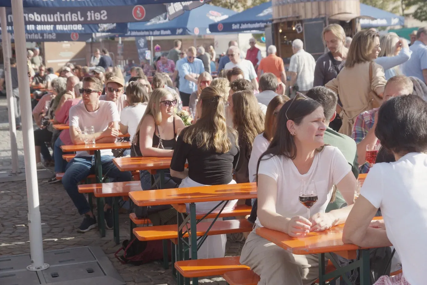 Volle Bierbänke auf dem Schlossplatz am ersten Samstag, vorne eine Frau mit Rotweinglas, dahinter Gäste bis zu den Ständen