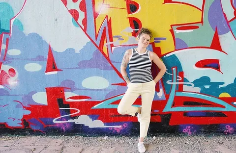 Lisa Knauer im gestreiften Top vor einer bunt besprühten Wand